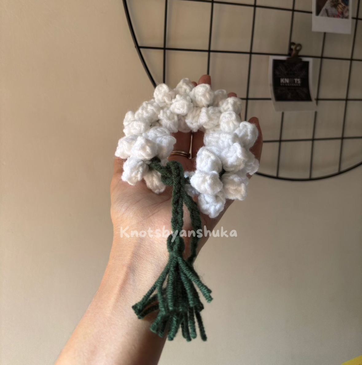 Hand holding a white gajra with green stems against a neutral background
