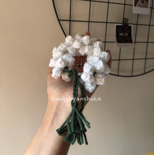 Hand holding a white gajra with green stems against a neutral background